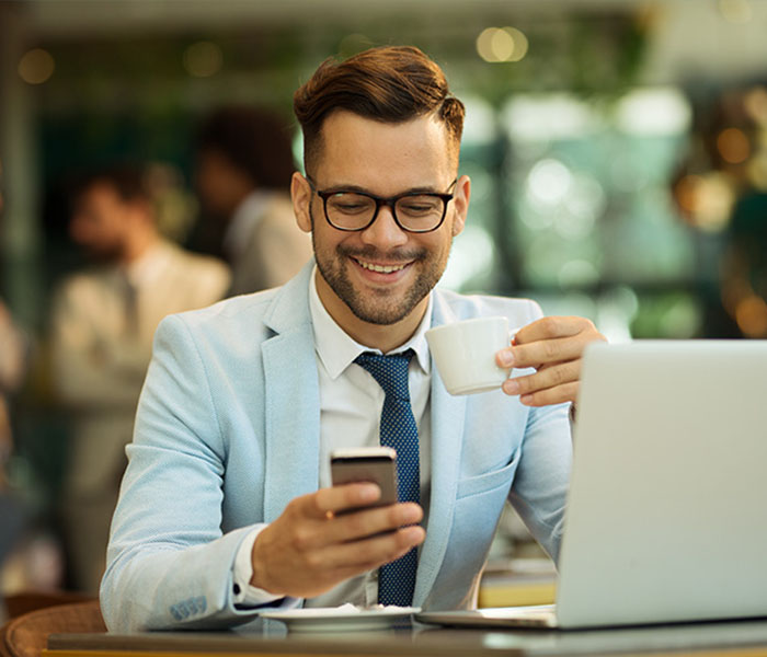 man with coffee out in public smiling at his phone